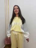 Primer plano de mujer vistiendo conjunto de chándal amarillo y gris con mensaje Amour en lentejuelas.